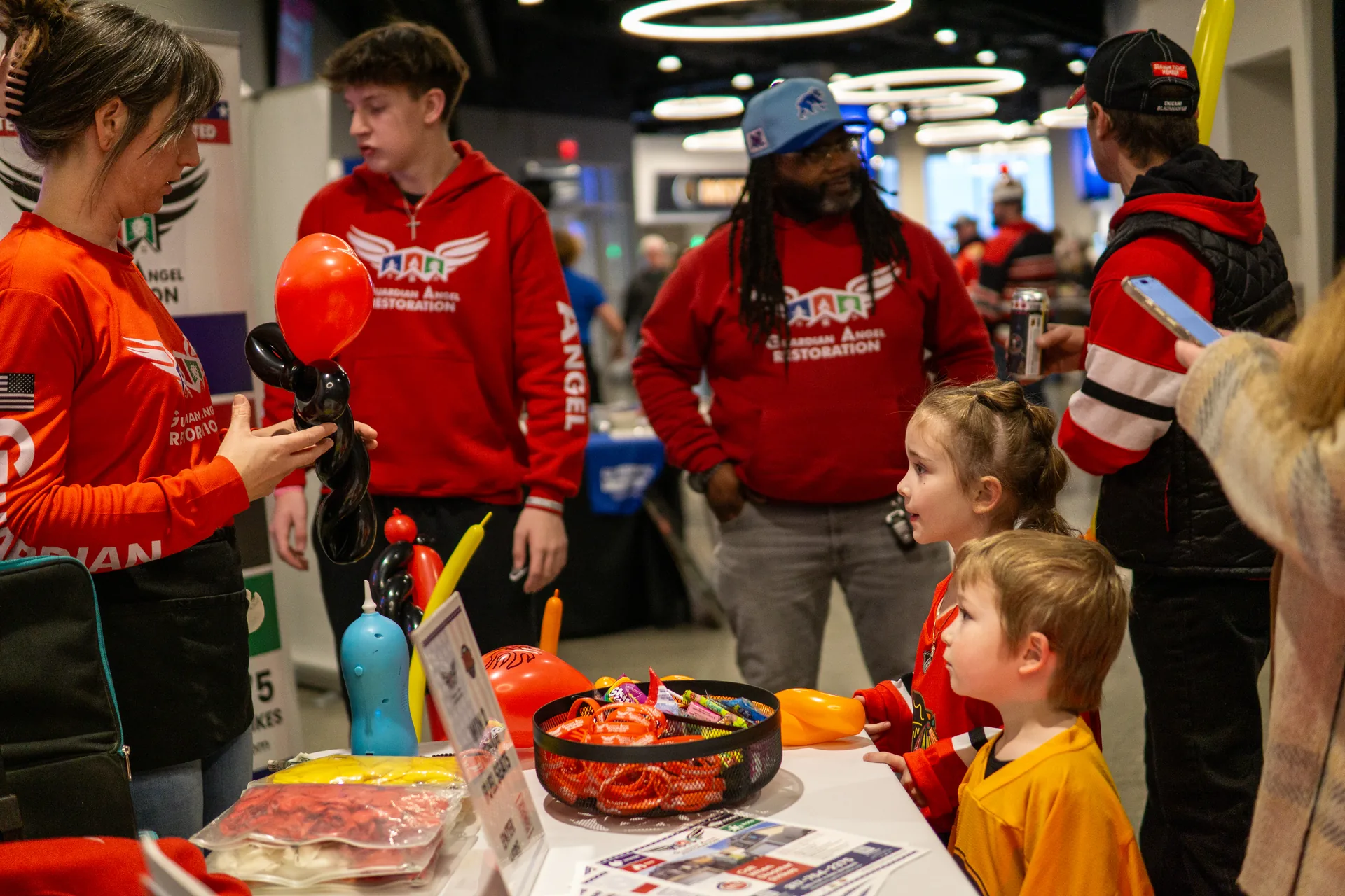 Guardian Angel crew member making balloon animals for a line of kids at the booth