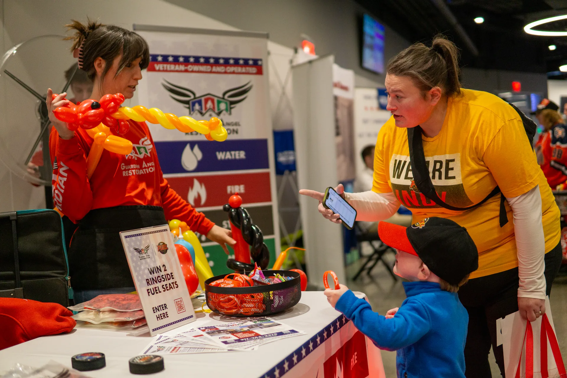 Crew making a balloon animal for a mom and toddler at the Guardian Angel booth