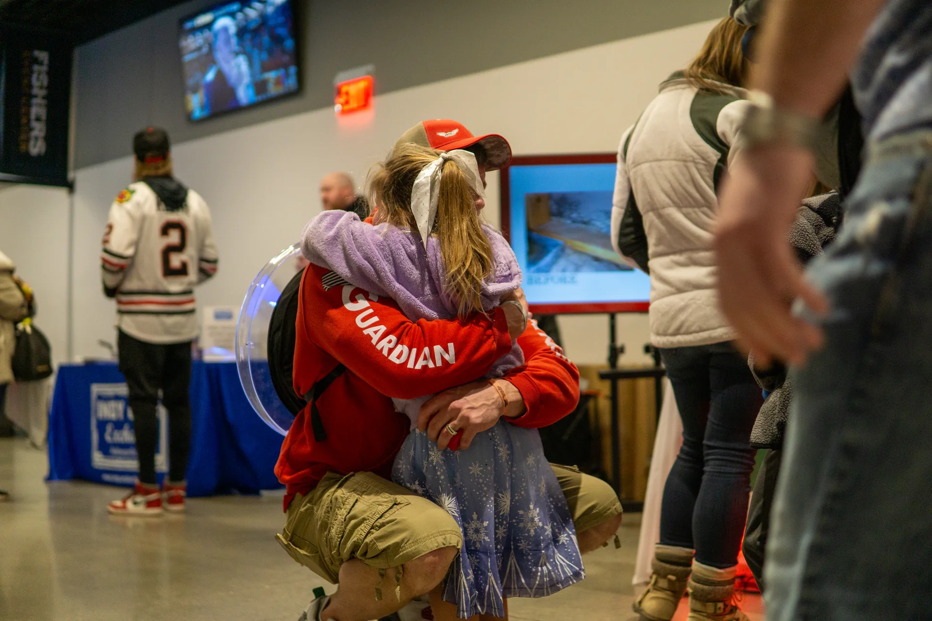 Back angle of Guardian Angel crew member hugging a little girl in a blue dress