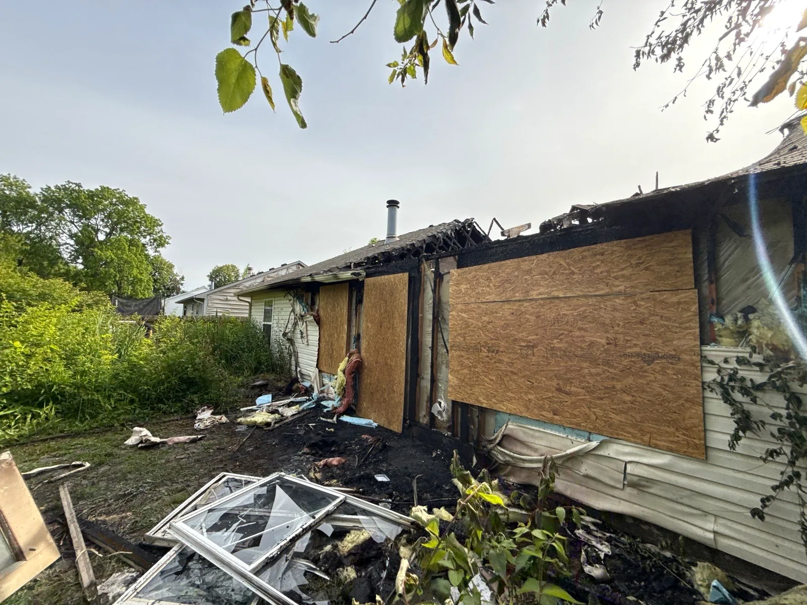 Rear window and door openings secured with OSB board-up after a house fire.
