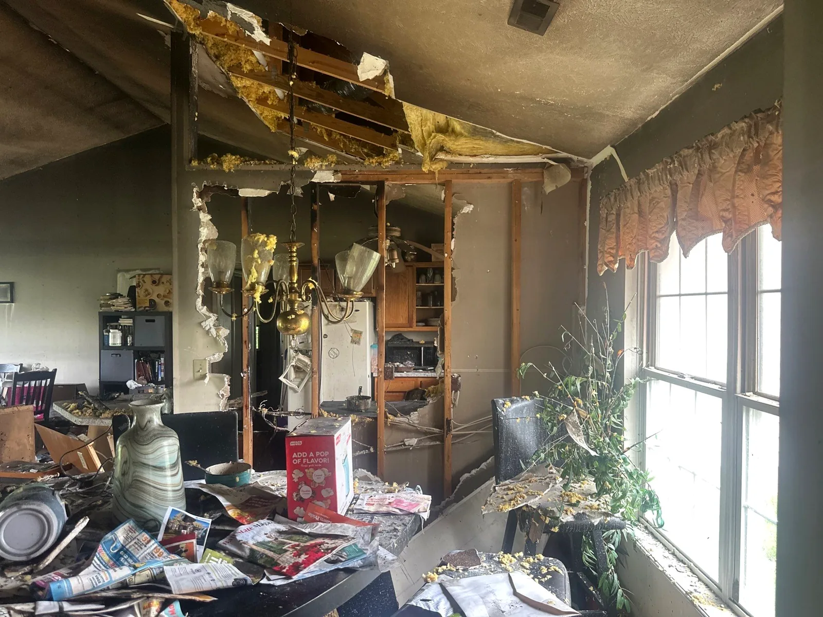 Fire-damaged dining room with charred wall framing exposed and the chandelier still in place.