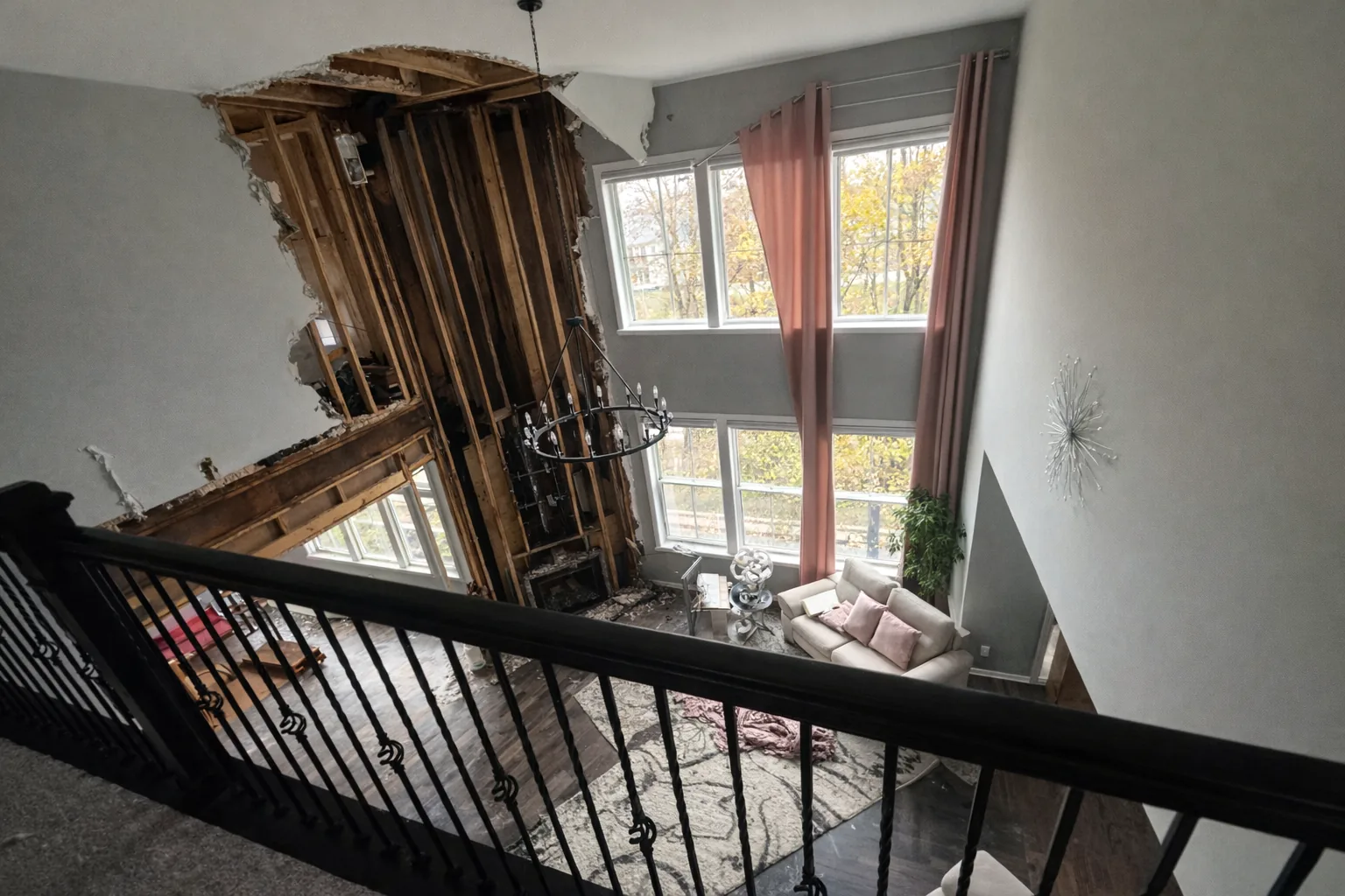View from an upstairs balcony of a two-story living room with drywall removed and charred framing exposed along the chimney chase.