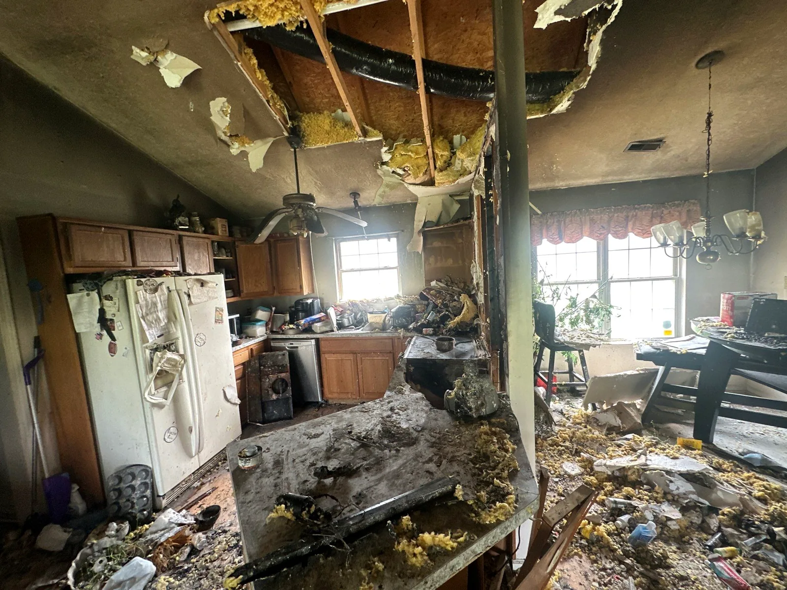 Kitchen gutted after a grease fire, with burned cabinet shells and insulation debris on the counters and floor.