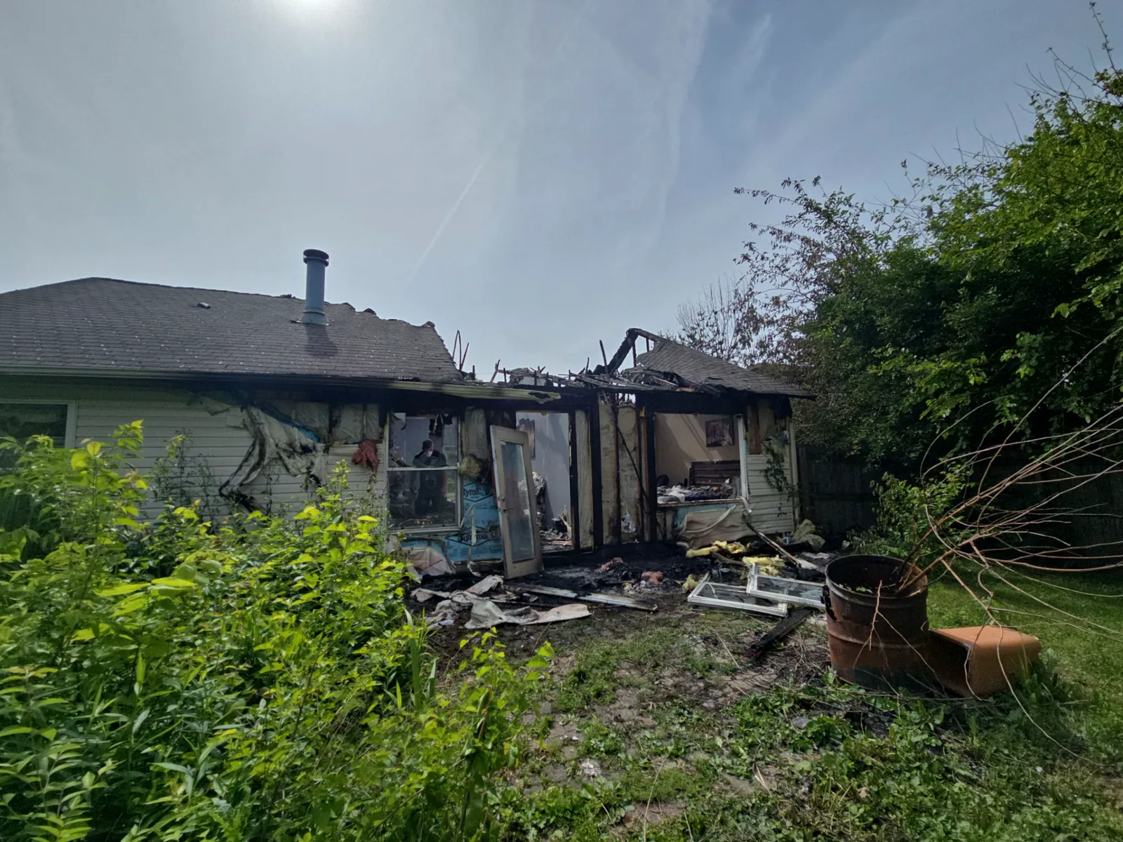 Rear exterior of a house with siding burned away and framing charred after a structure fire.
