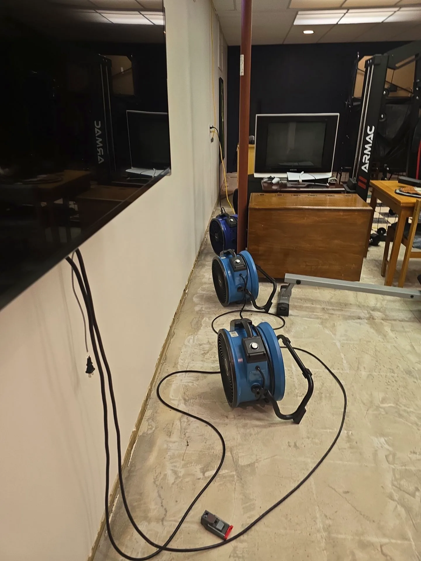 Three air movers drying a basement wall where baseboard has been removed.