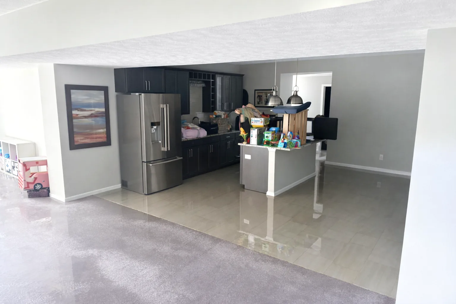Basement kitchenette with standing water shining across tile and soaked carpet at the edge.