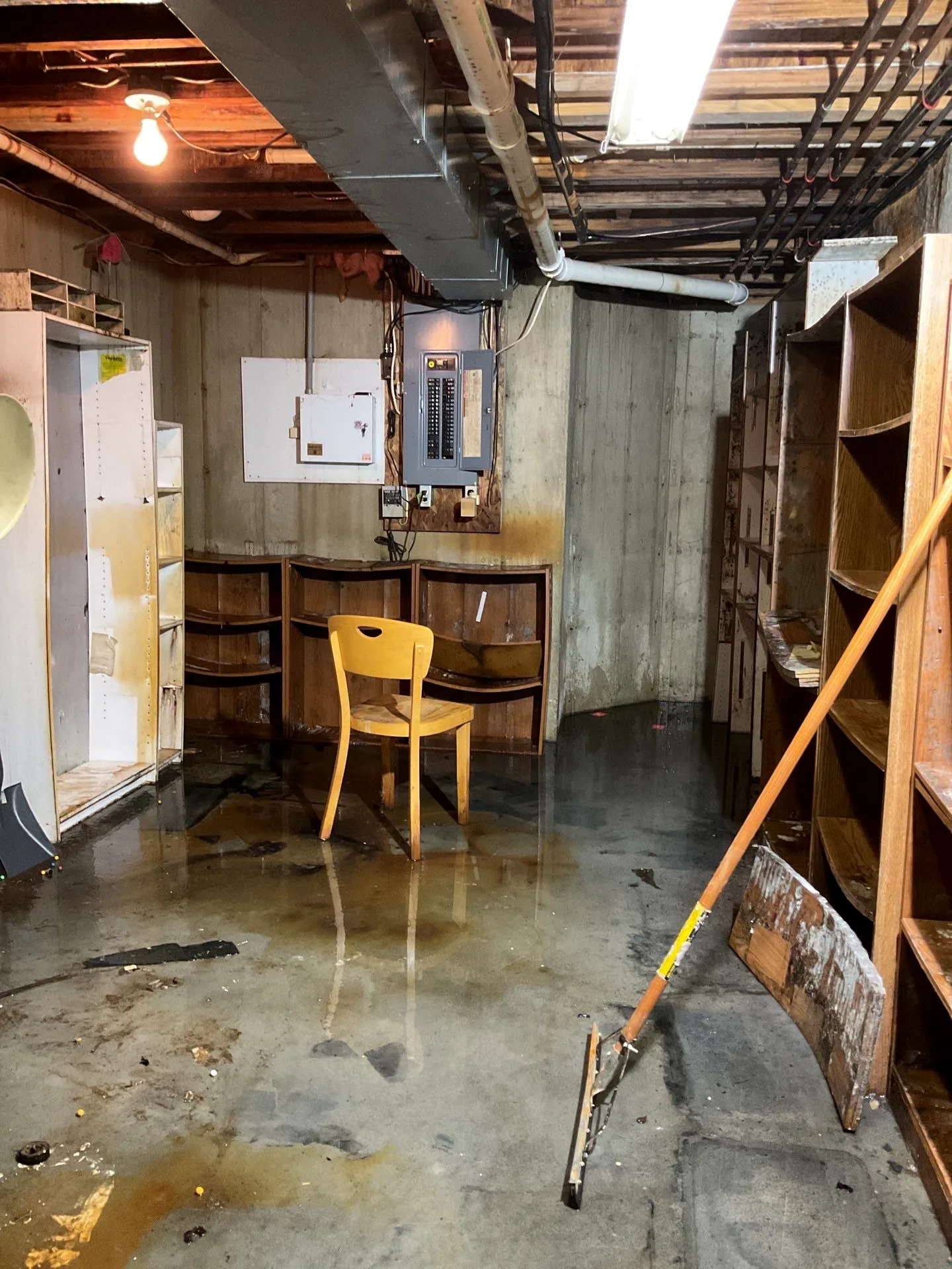 Standing water across a utility basement floor with a squeegee staged for cleanup.