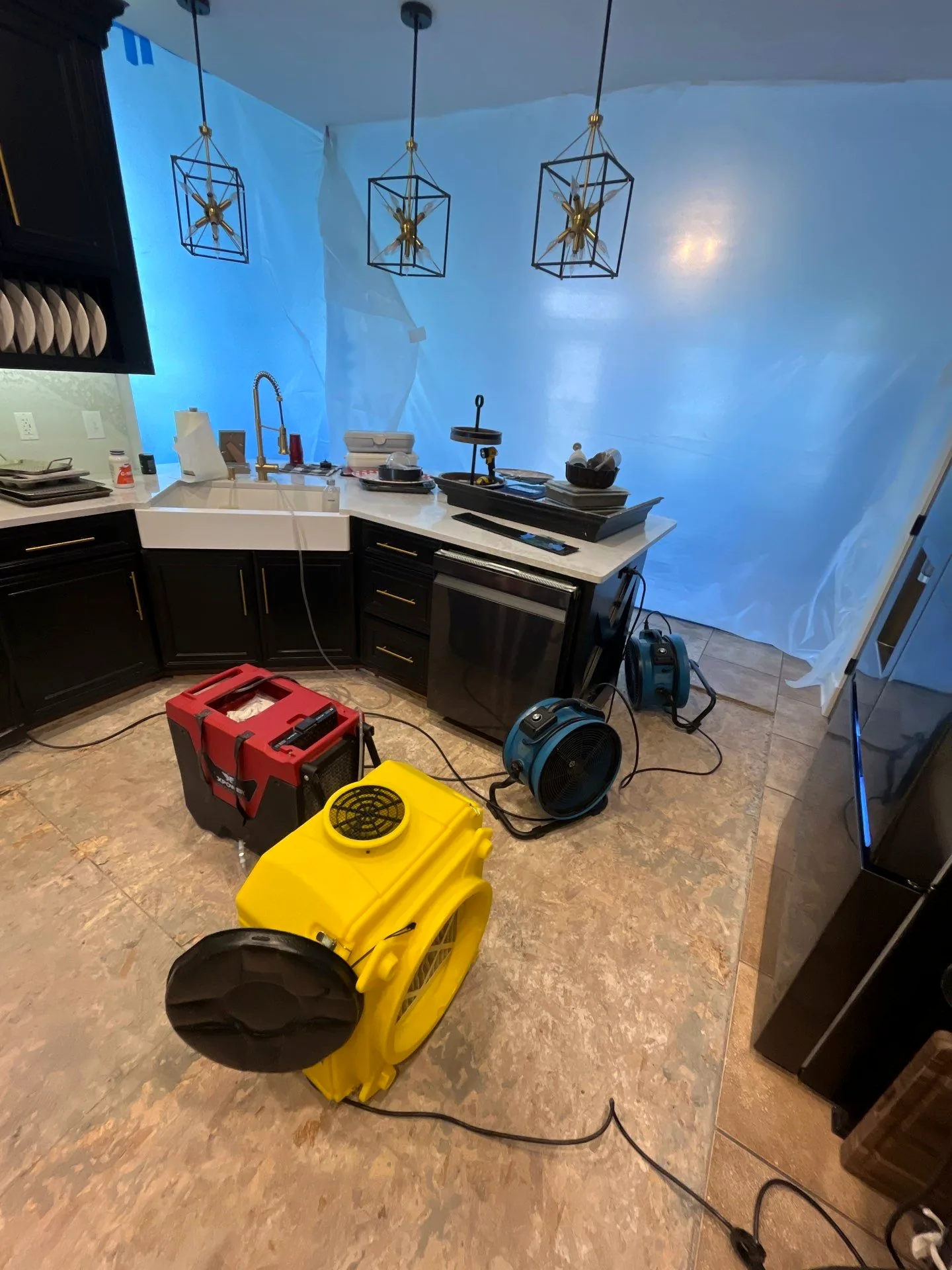 Kitchen sealed behind plastic containment with a dehumidifier and air movers drying the exposed subfloor.