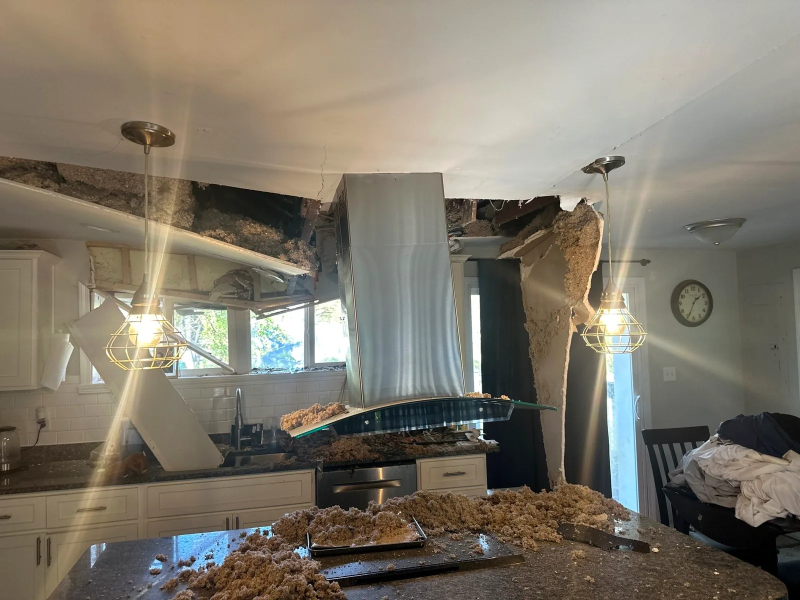 Sunlight streaming through a collapsed kitchen ceiling with insulation heaped across the island after a roof failure.