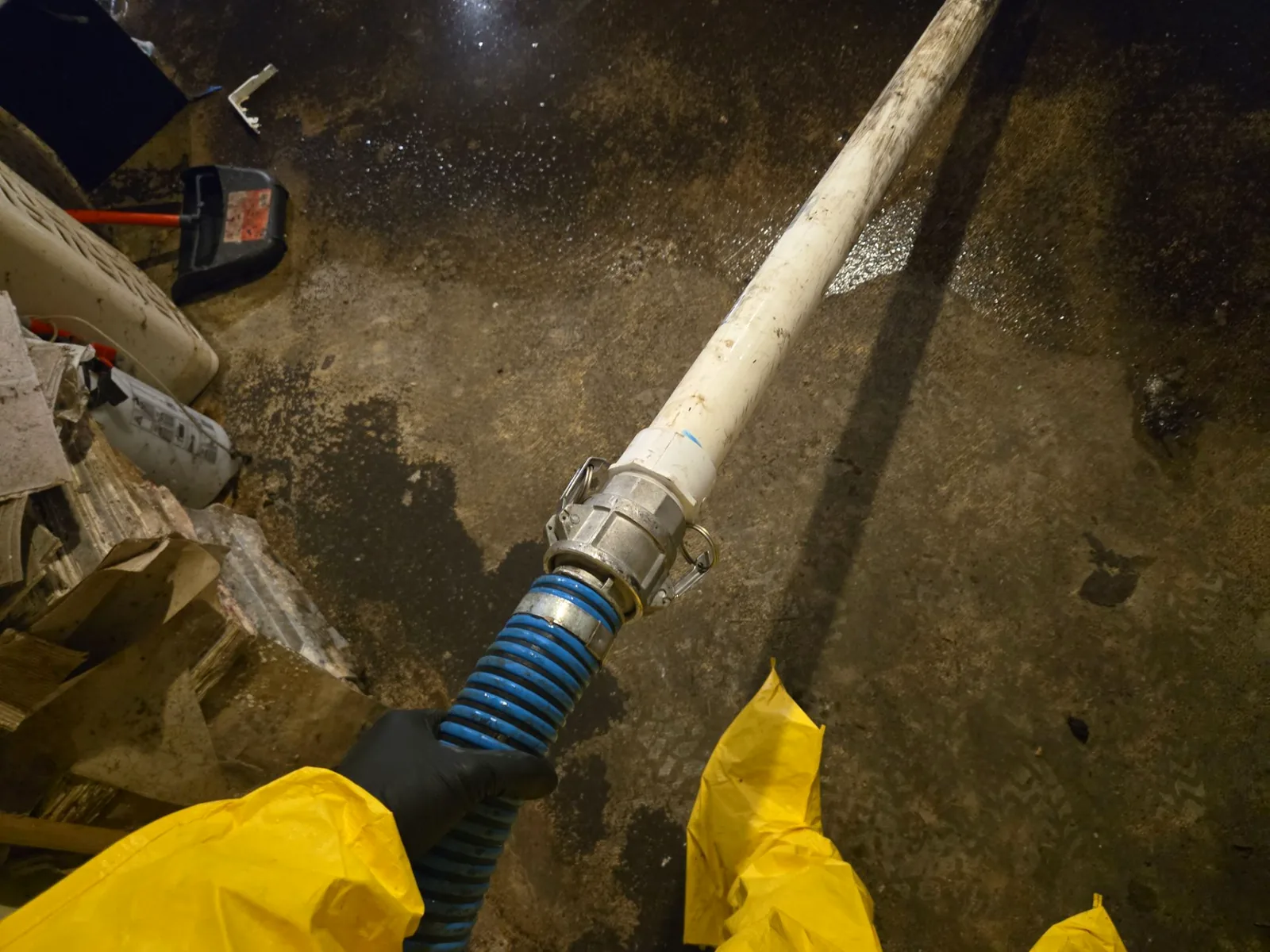 Gloved hand connecting a camlock suction hose to discharge pipe during basement water removal.