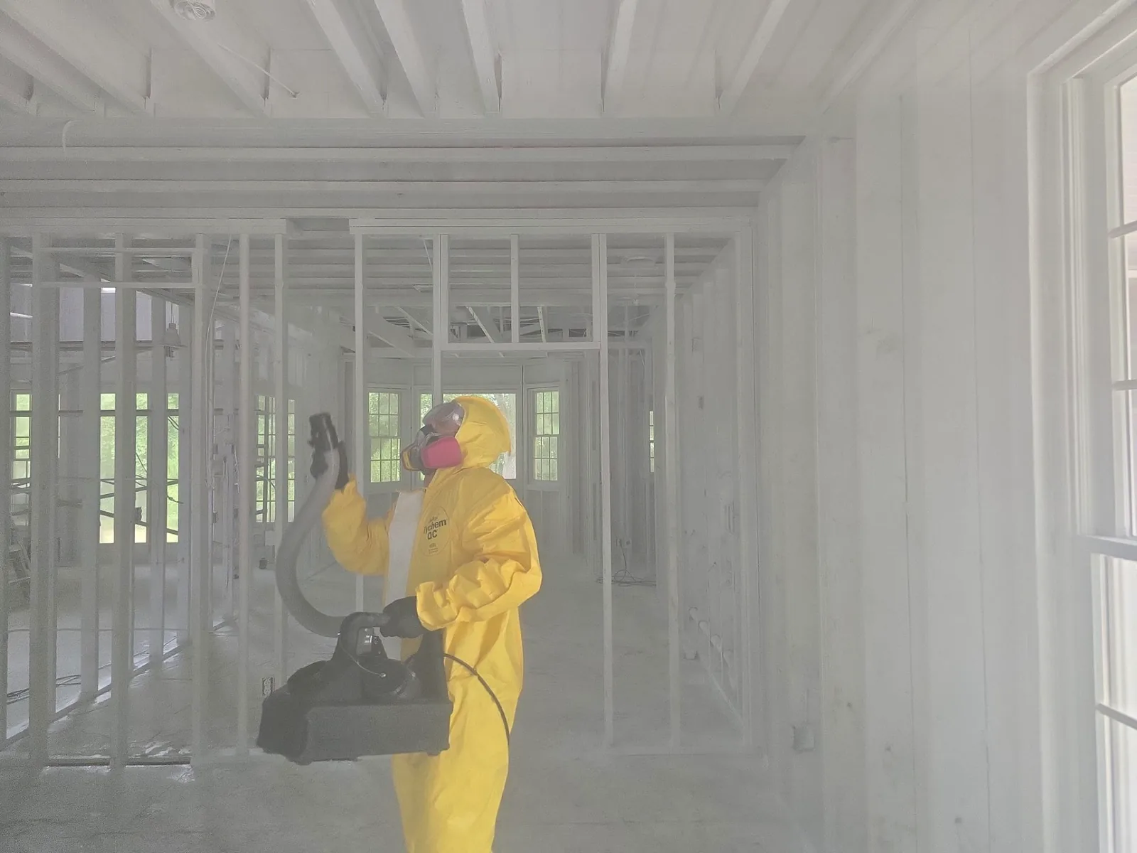Technician in a yellow protective suit fogging sealed framing during remediation after water damage.