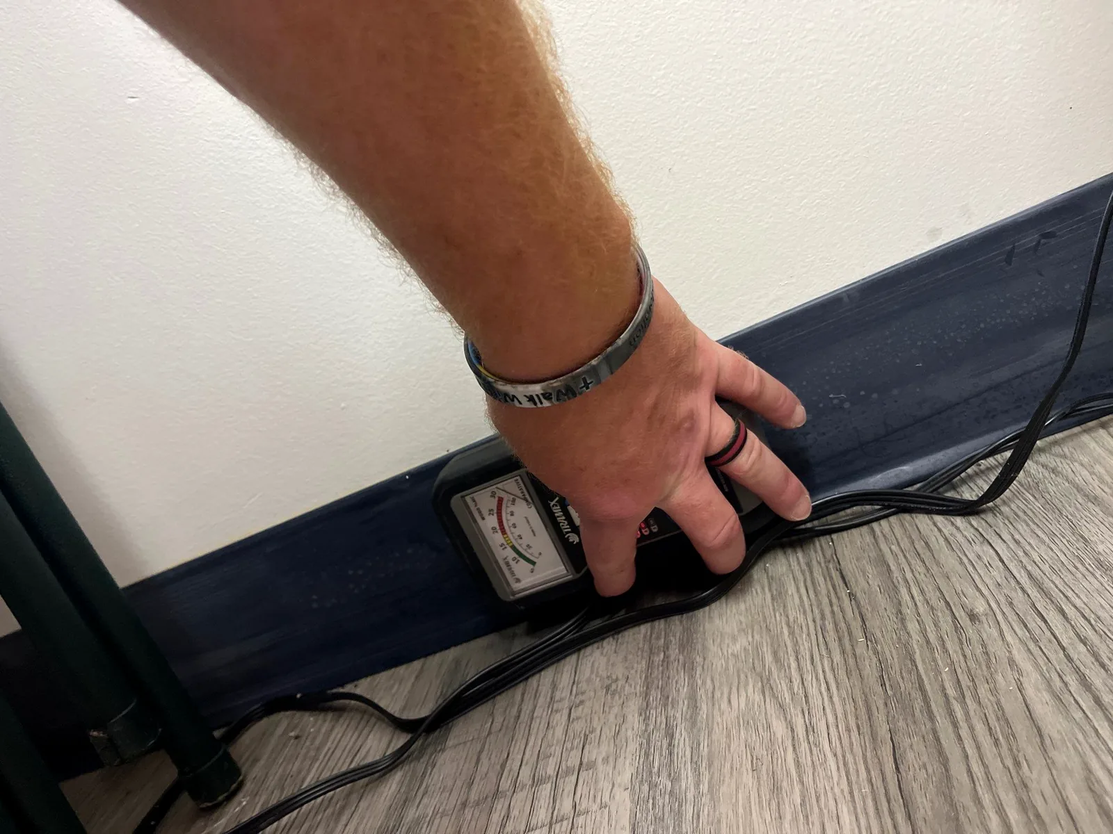 Technician pressing a moisture meter against a painted baseboard to map water migration.