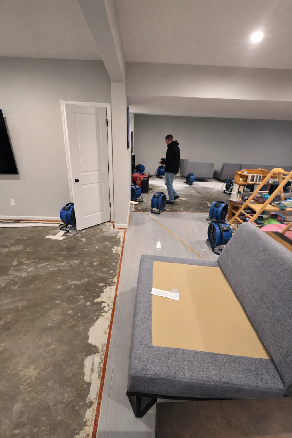 Technician positioning a ring of air movers on exposed concrete after wet carpet was removed from a basement.