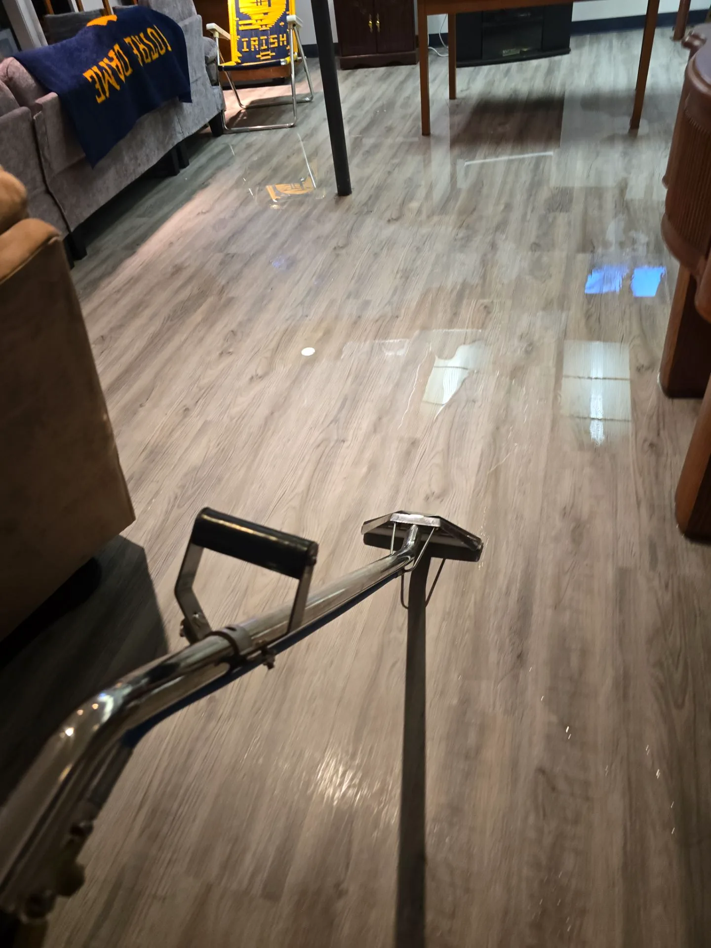 Extraction wand pulling standing water off a flooded basement plank floor.
